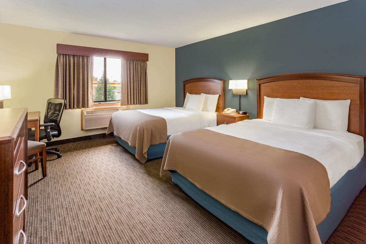 A hotel room with two beds, a desk, a chair, and a window with curtains.
