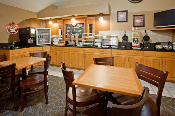 A hotel kitchen with wooden cabinets, a refrigerator, a coffee machine, and a chalkboard menu. - AmericInn by Wyndham Princeton MN (Princeton)
