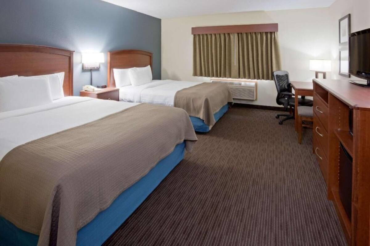 A hotel room with two beds, a desk, a chair, a television, and an air conditioning unit.