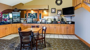 Une cuisine avec des meubles en bois, une table à manger avec des chaises, une machine à café et un téléviseur fixé au mur.