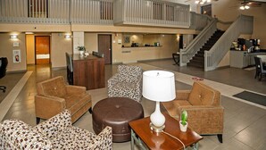 A spacious lobby with a high ceiling, a central seating area with patterned sofas and ottomans, a reception desk, and a staircase leading to an upper level. - Quality Inn near Medical Center (Rochester)