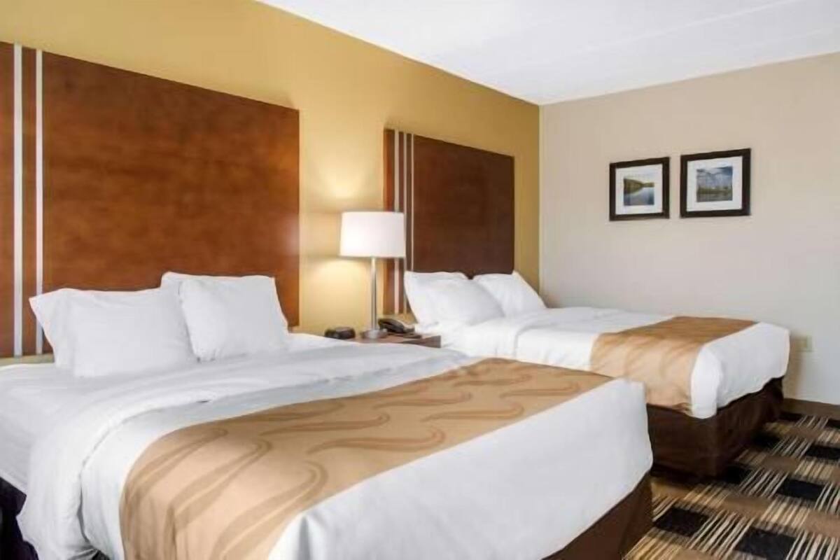 A hotel room with two beds, a nightstand with a lamp, and two framed pictures on the wall.