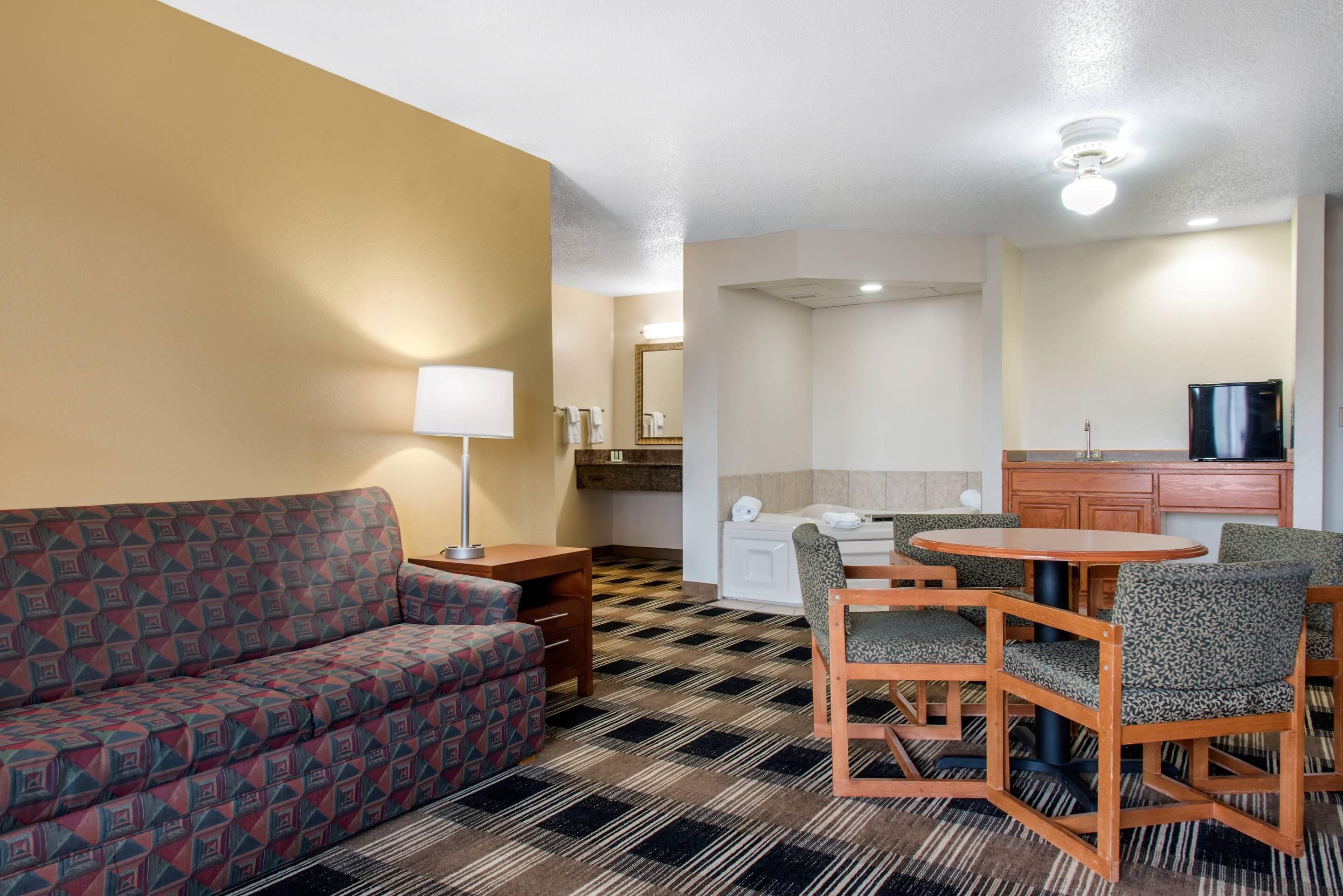 A hotel room with a sofa, a dining table with chairs, a small kitchenette, and a television.