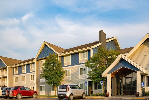 A row of multi-story residential buildings with a central entrance, parking spaces, and a handicap-accessible sign.