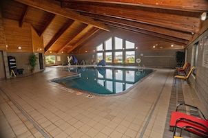 Una piscina interior con techo de madera y amplios ventanales.