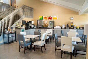 Un restaurante con una escalera, mesas, sillas, una cafetera y un refrigerador.