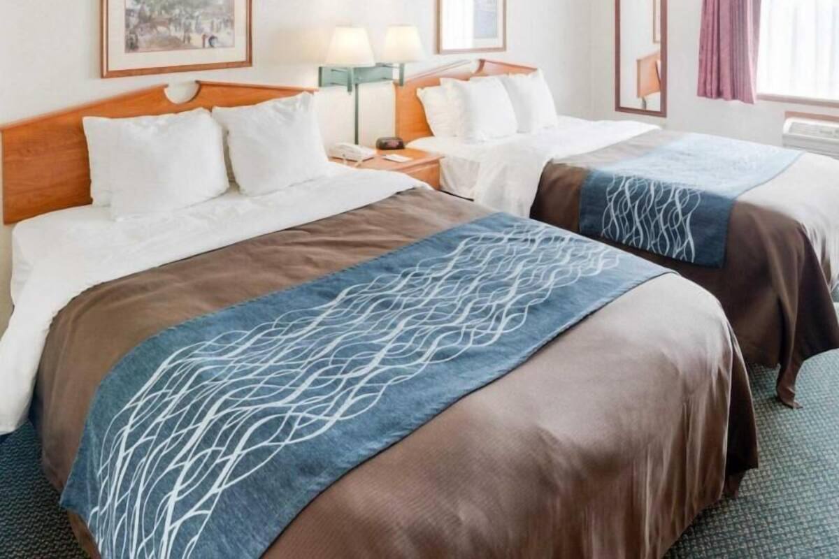 A hotel room with two beds, a nightstand, a lamp, and a framed picture on the wall.