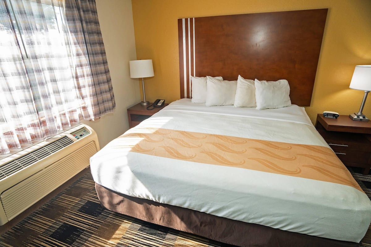 A hotel room with a large bed, two bedside tables, a heater, and a window with curtains.
