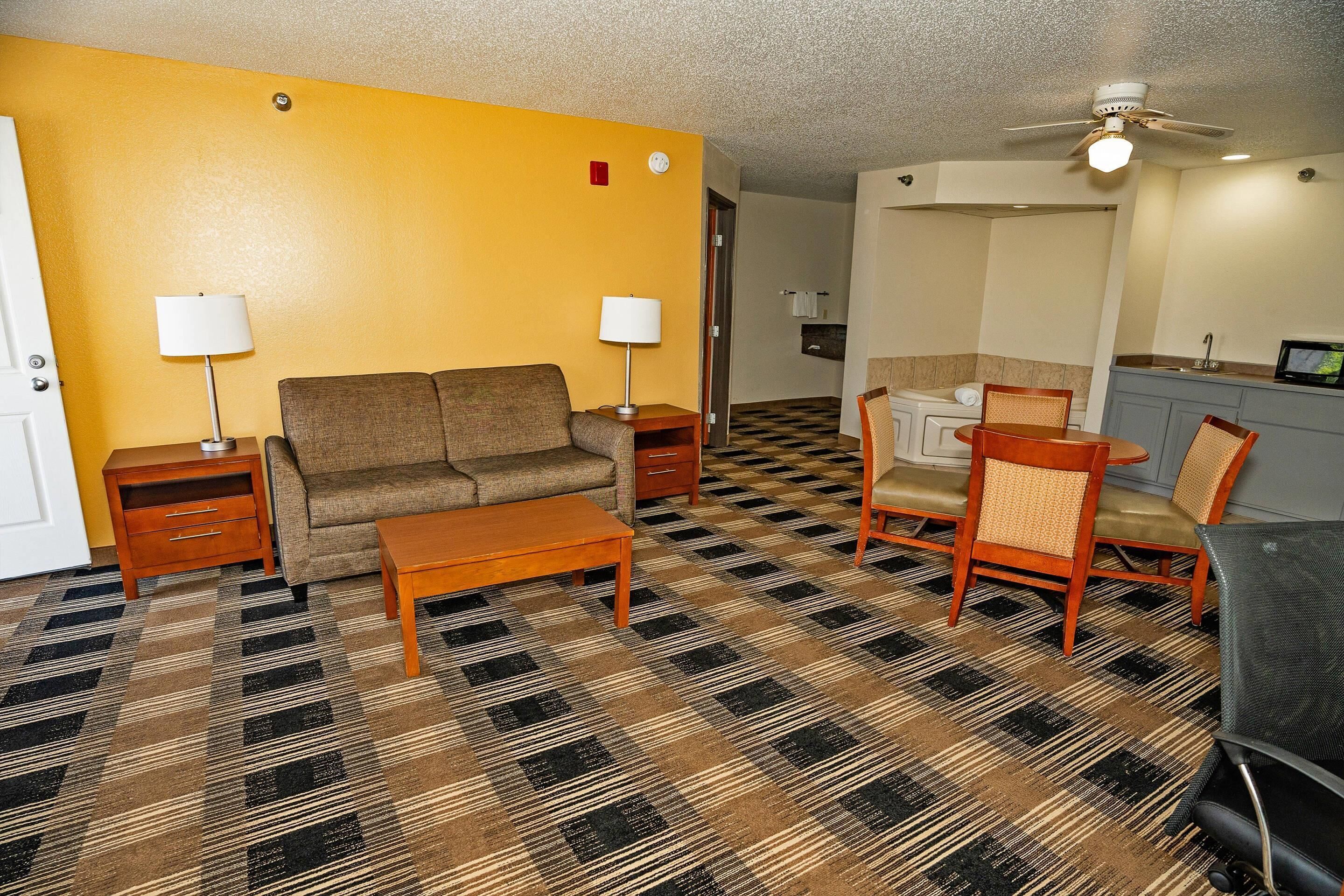 A living room with a sofa, coffee table, and two chairs, a patterned carpet, and a ceiling fan.