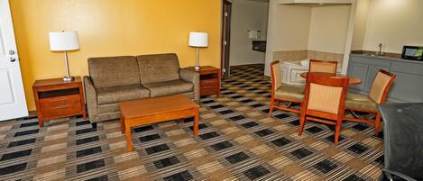 A living room with a sofa, coffee table, and two chairs, a patterned carpet, and a ceiling fan.