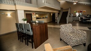 A spacious living area with a wooden dining table, bar stools, and a patterned armchair. A staircase leads to an upper level with a balcony. - Quality Inn near Medical Center (Rochester)