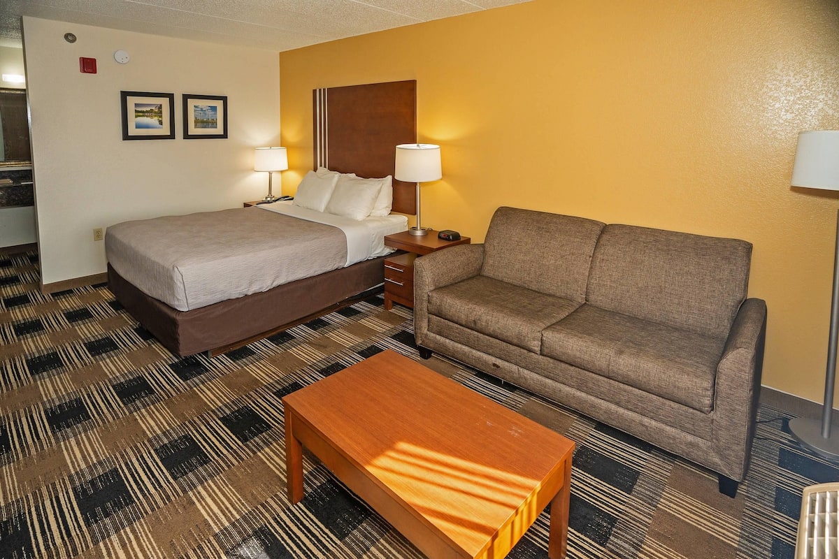 A hotel room with a bed, a sofa, a coffee table, and two lamps.