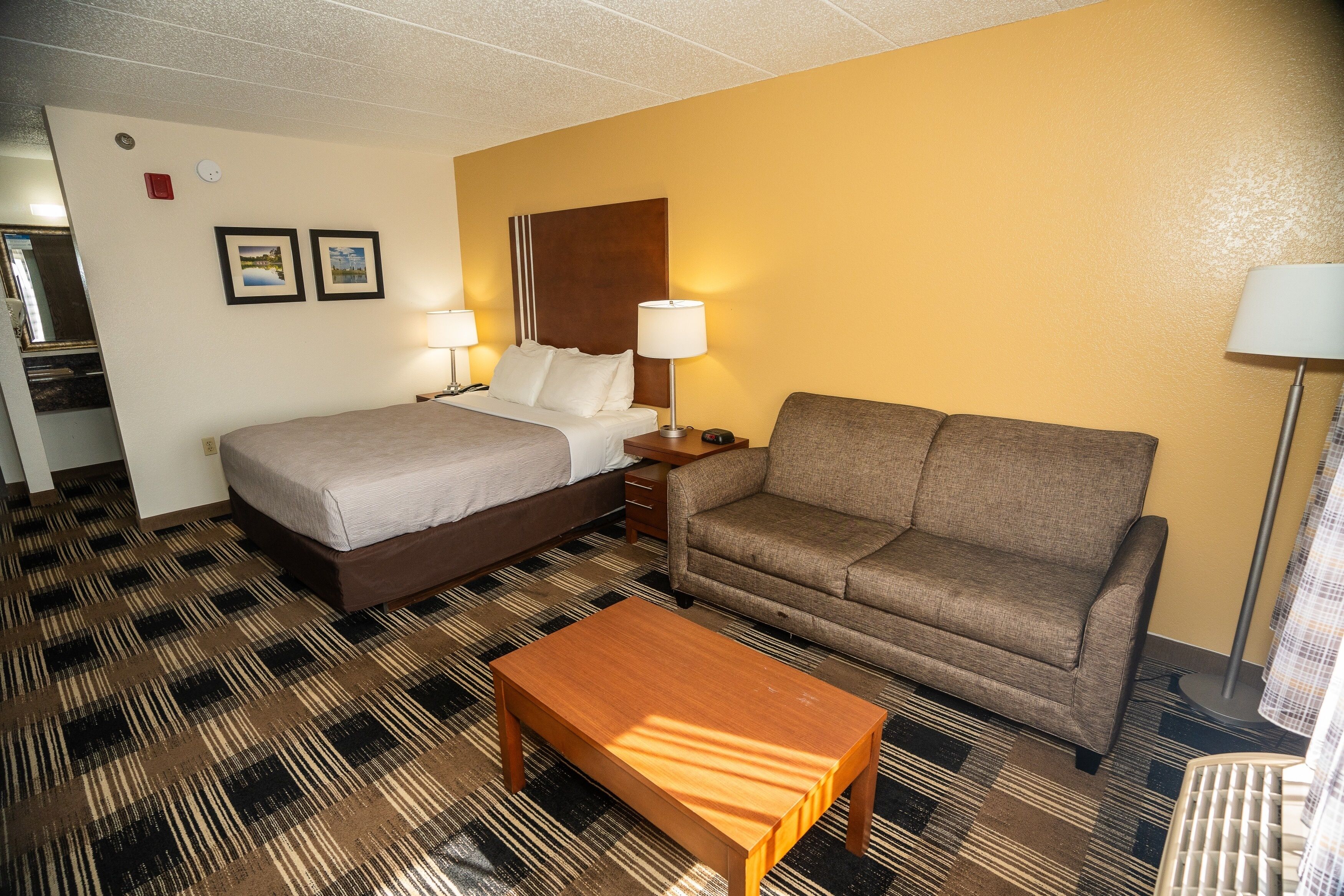 Una habitación de hotel con una cama, un sofá, una mesa de centro y dos lámparas.