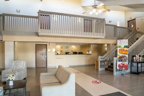 A hotel lobby with a reception desk, seating area, and a staircase leading to an upper level.