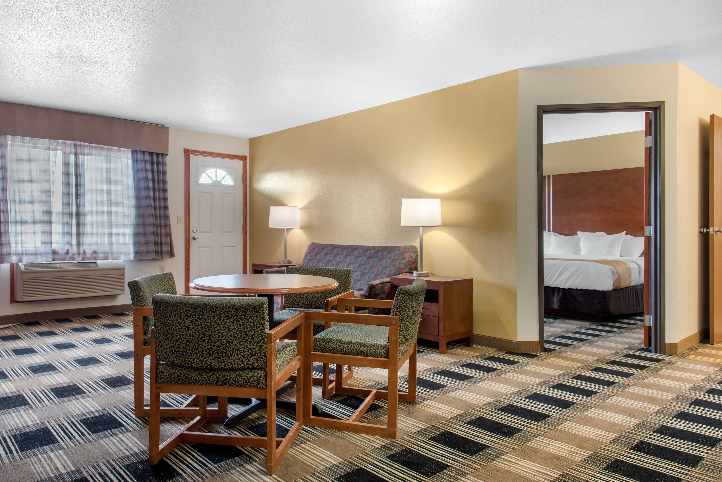 Una habitación de hotel con piso a cuadros, una mesa redonda con sillas, un sofá, una cama y un espejo.