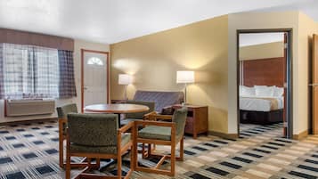 Una habitación de hotel con piso a cuadros, una mesa redonda con sillas, un sofá, una cama y un espejo.