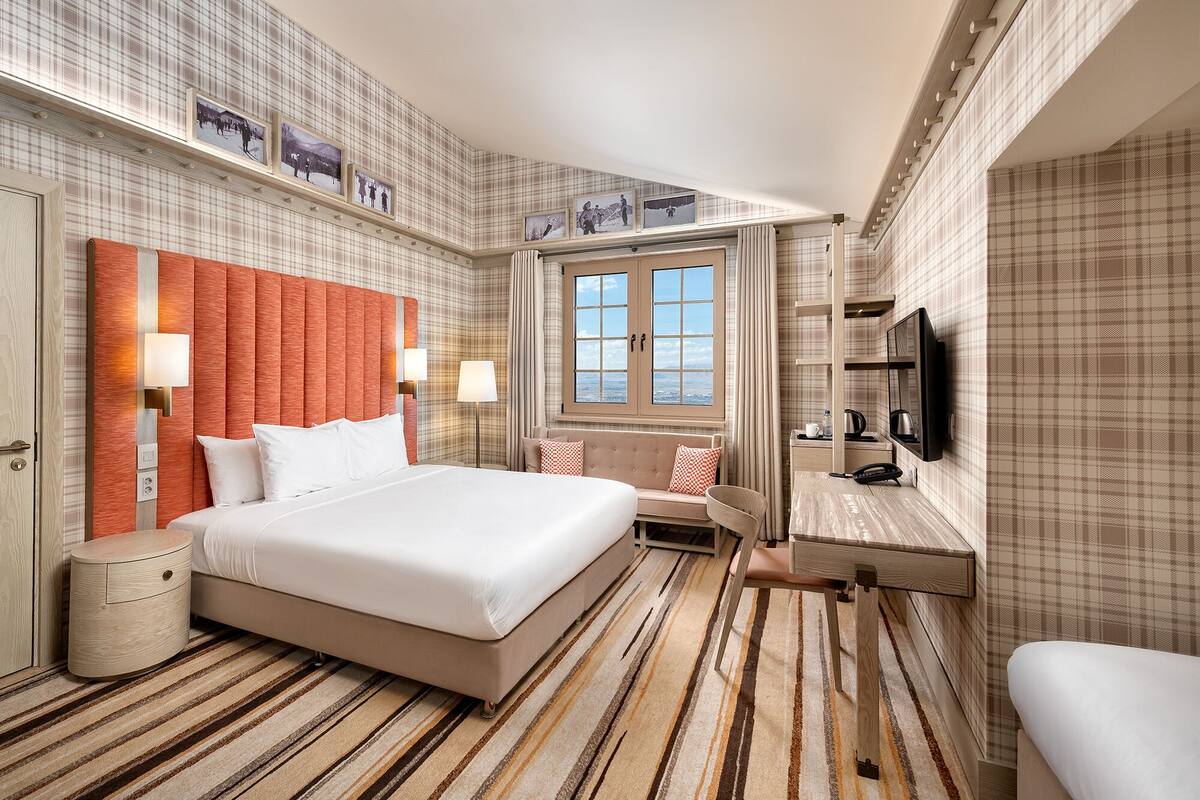 A hotel room with a large bed, a TV, a desk, and a window with a view.