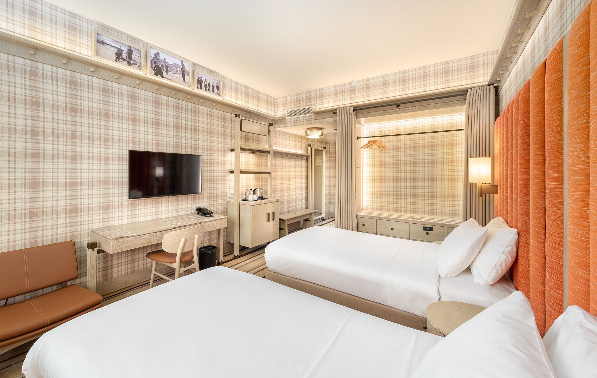 Habitación de hotel con dos camas, un escritorio, una silla, un televisor y una ventana con cortinas.