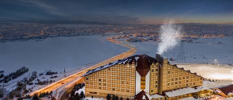 Ein großes Hotel mit markanter Architektur, eingebettet in eine verschneite Landschaft mit Blick auf einen Fluss und entfernte Stadtlichter.
