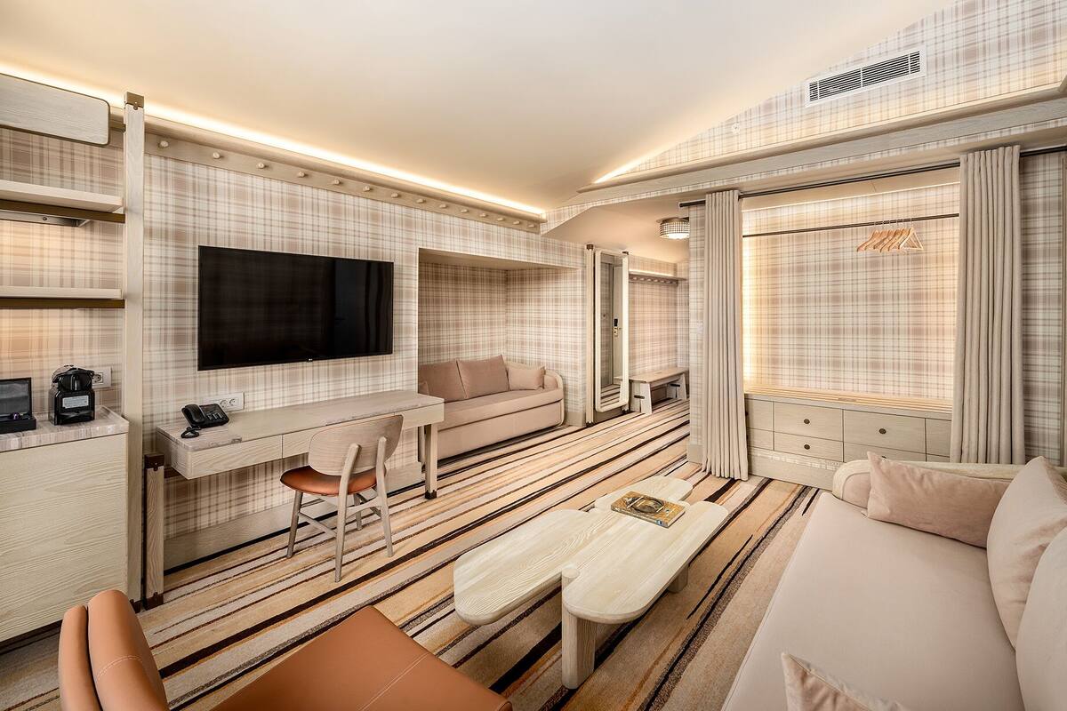 A modern hotel room with a flat-screen TV, a sofa, a dining table, and a mirror.