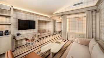 A modern hotel room with a flat-screen TV, a sofa, a dining table, and a mirror.