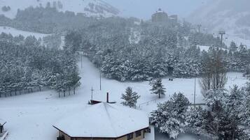 A snow-covered building with a flat roof, surrounded by trees and a parking area with cars.
