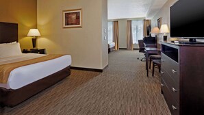 A hotel room with a large bed, a desk with a chair, a television, and a lamp.