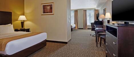 A hotel room with a large bed, a desk with a chair, a television, and a lamp.