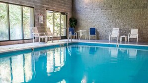 Piscina interna com água azul cristalina, rodeada por espreguiçadeiras brancas e uma parede de tijolos.