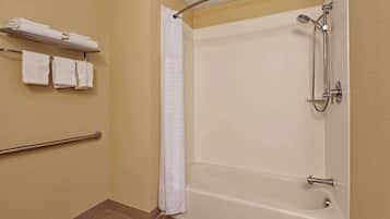 A bathroom with a bathtub, shower, and handrails.