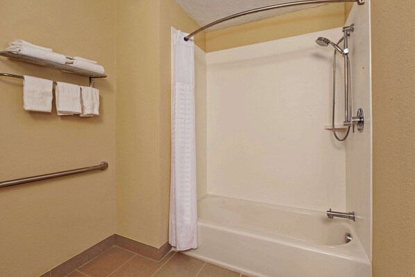 A bathroom with a bathtub, shower, and handrails.