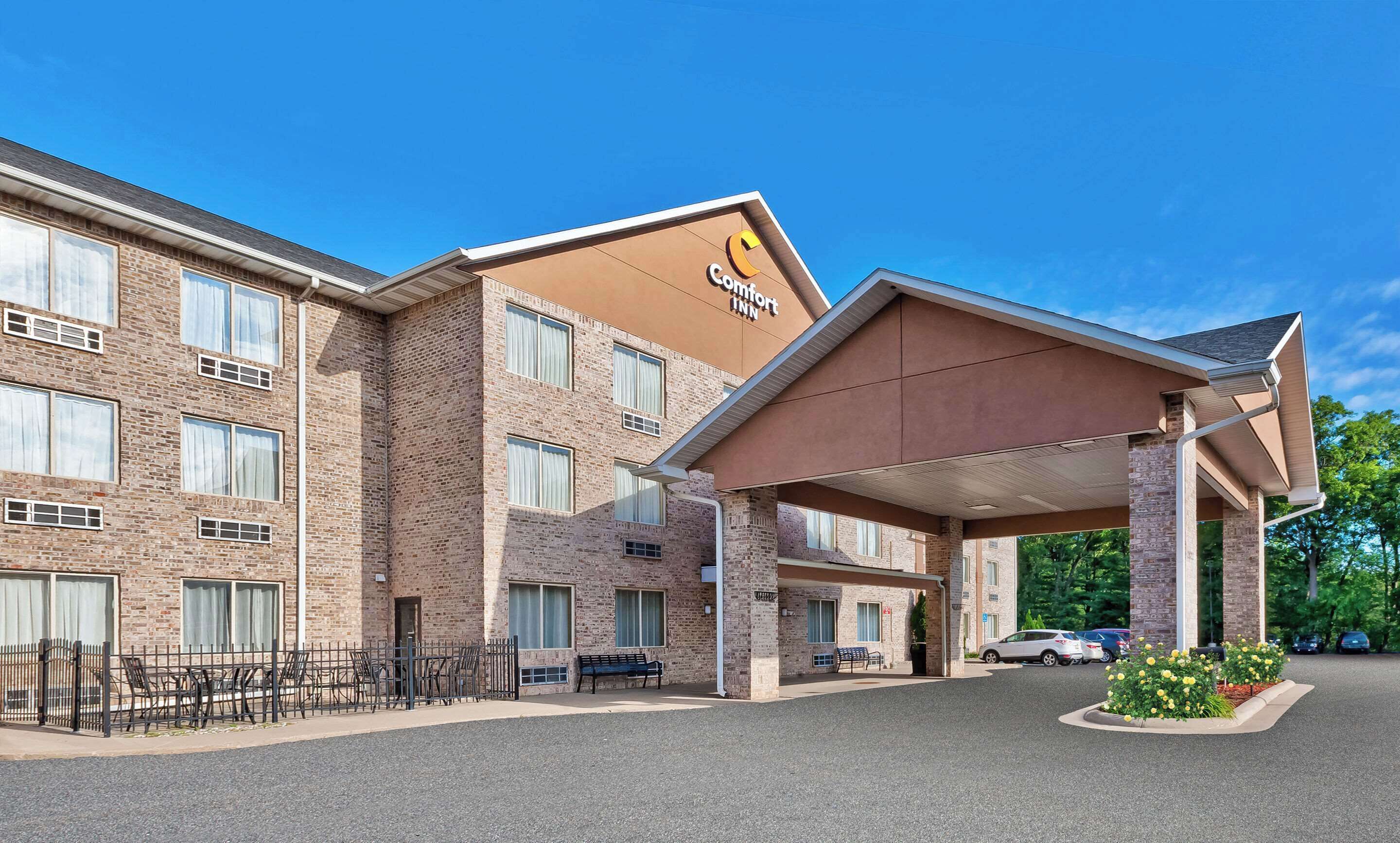 A Comfort Inn hotel with a brick facade, a covered entrance, and a parking area with cars and a flower bed.