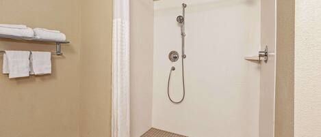 Eine Dusche mit Duschbrause, Wandarmatur und Handtuchhalter mit gefalteten Handtüchern.