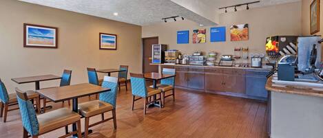 Un comedor de hotel con mesas y sillas de madera, una isla central con una máquina de café y cuadros en las paredes.