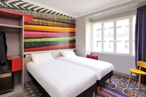 Habitación de hotel con dos camas, un armario rojo, un papel tapiz estampado, una ventana con cortinas y una alfombra con diseño.