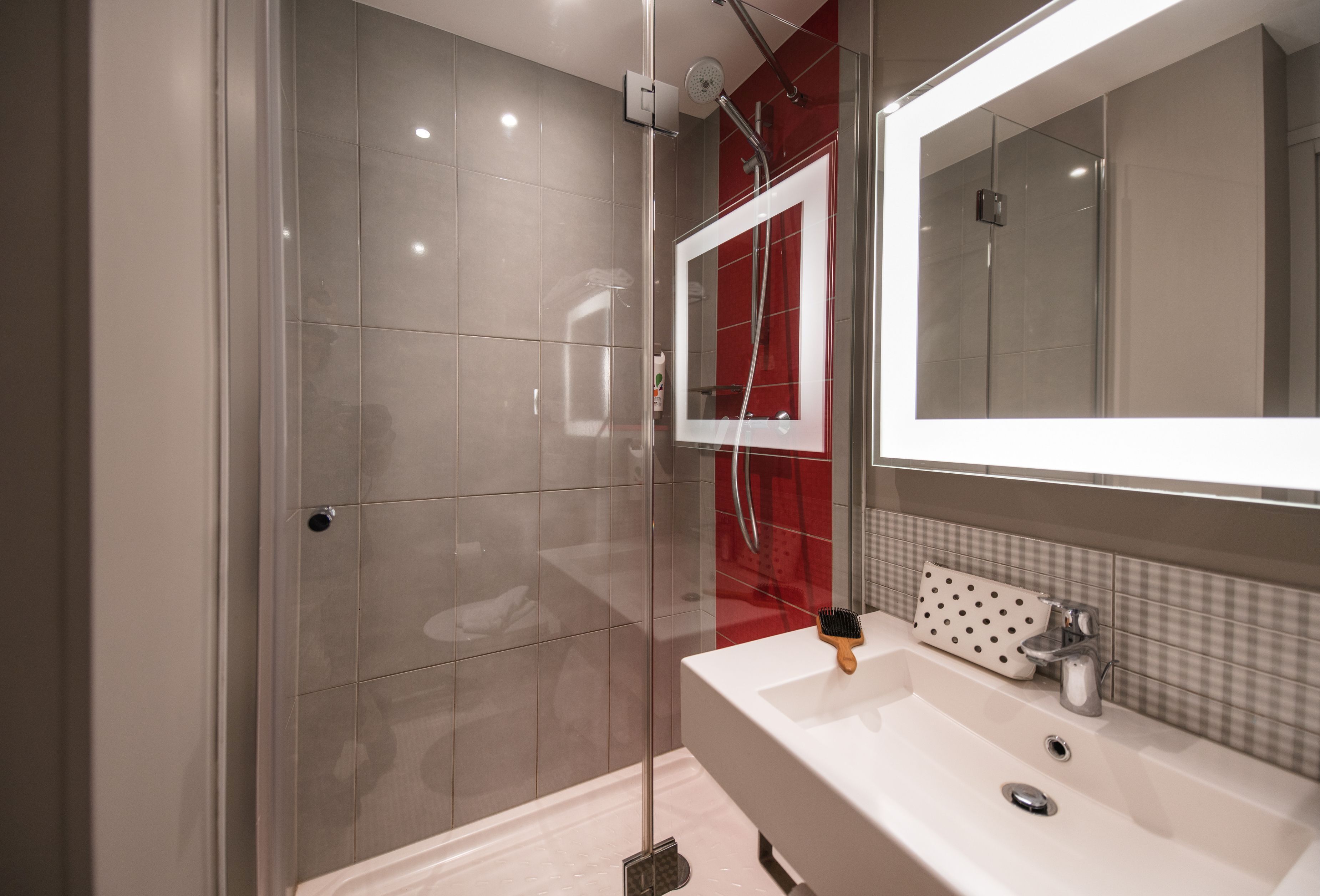 Un baño moderno con cabina de ducha de vidrio, un lavabo blanco y un espejo con marco rojo.