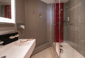 Un baño moderno con ducha de vidrio, lavamanos blanco y espejo sobre él.