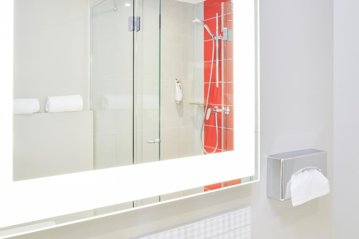 Un baño moderno con cabina de ducha de vidrio, dispensador de toallas y piso de baldosas.