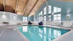 Una piscina interior con agua cristalina, vigas de madera en el techo y ventanas amplias.