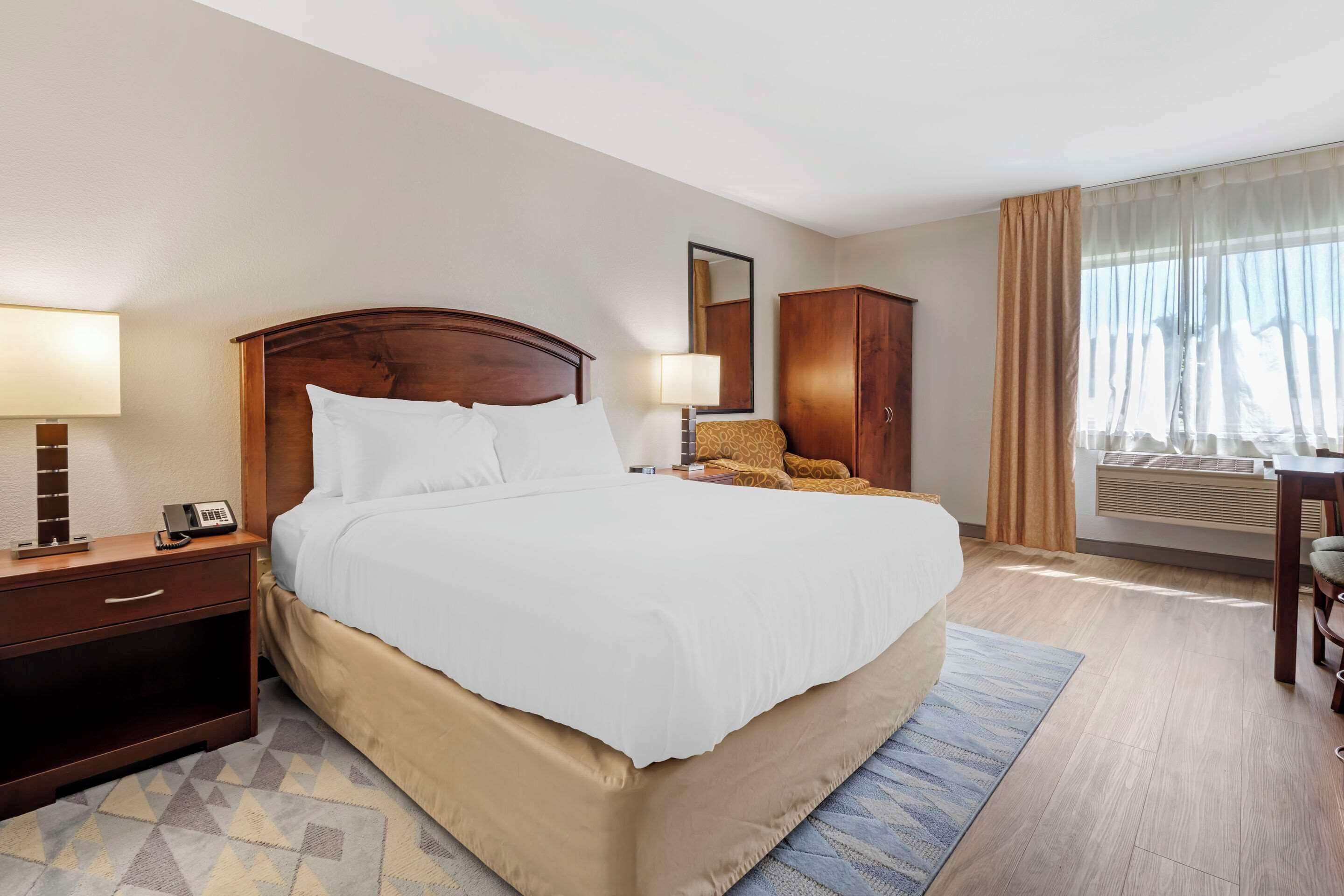 A hotel room with a large bed, bedside tables, a wardrobe, a desk, and a window with curtains.
