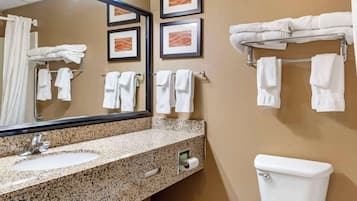 A bathroom with a granite countertop sink, a mirror, a toilet, and multiple towel racks with folded towels.