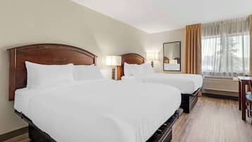 Een hotelkamer met twee tweepersoonsbedden, een bureau, een stoel, een spiegel en een raam met gordijnen.