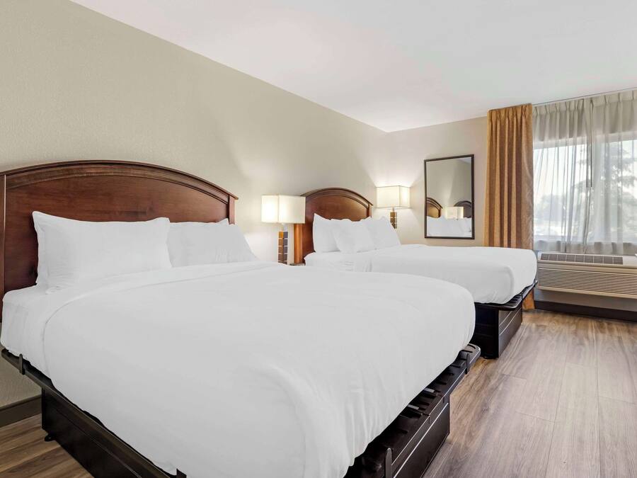 Een hotelkamer met twee tweepersoonsbedden, een bureau, een stoel, een spiegel en een raam met gordijnen.