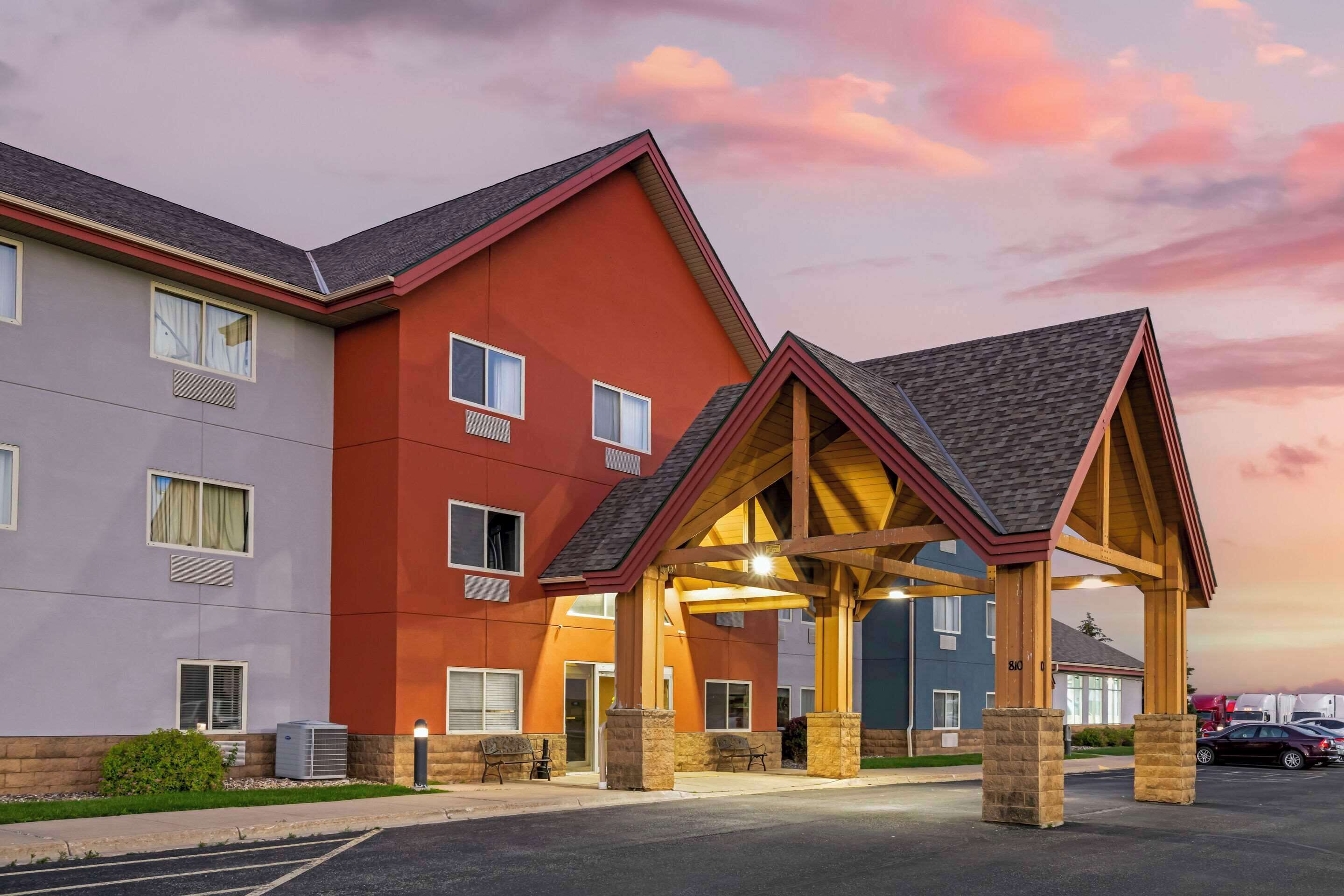 A multi-story hotel with a red and grey facade, a covered entrance, and a parking lot.