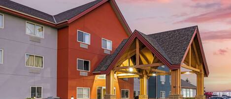 A multi-story hotel with a red and grey facade, a covered entrance, and a parking lot.