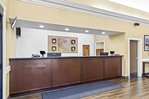 A reception desk with a modern design, a large wall-mounted artwork, and a wooden door in the background. - Comfort Suites Lake Jackson Clute (Lake Jackson)
