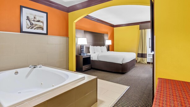 Une chambre d’hôtel avec une grande baignoire, un lit avec du linge de maison blanc, deux lampes de chevet et un tableau encadré au mur.