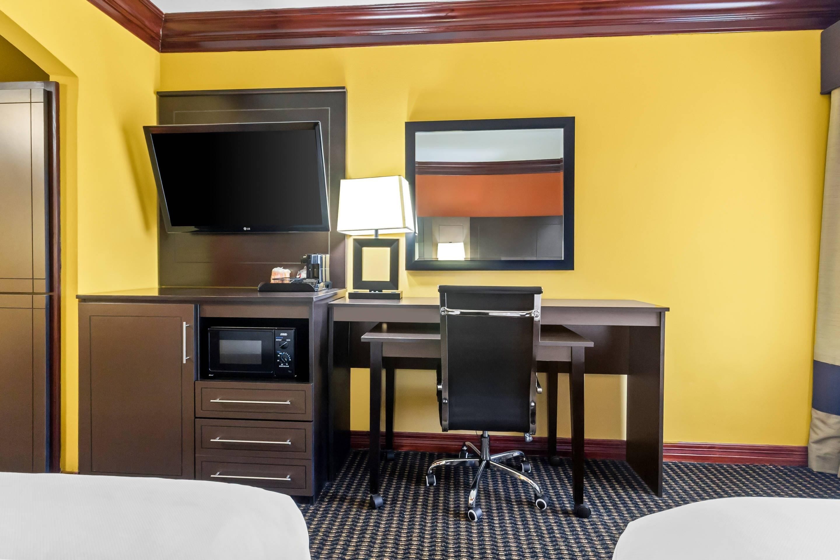A hotel room with a bed, a desk with a chair, a flat-screen TV, a microwave, and a lamp.