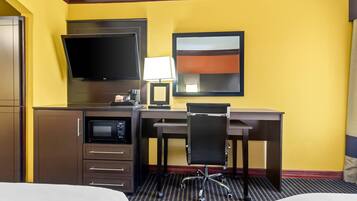 Habitación de hotel con cama, escritorio con silla, televisor de pantalla plana, microondas y lámpara.
