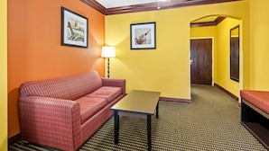 Une chambre d’hôtel avec un canapé rouge, une petite table, deux tableaux encadrés accrochés aux murs, une lampe et un tapis à motifs.